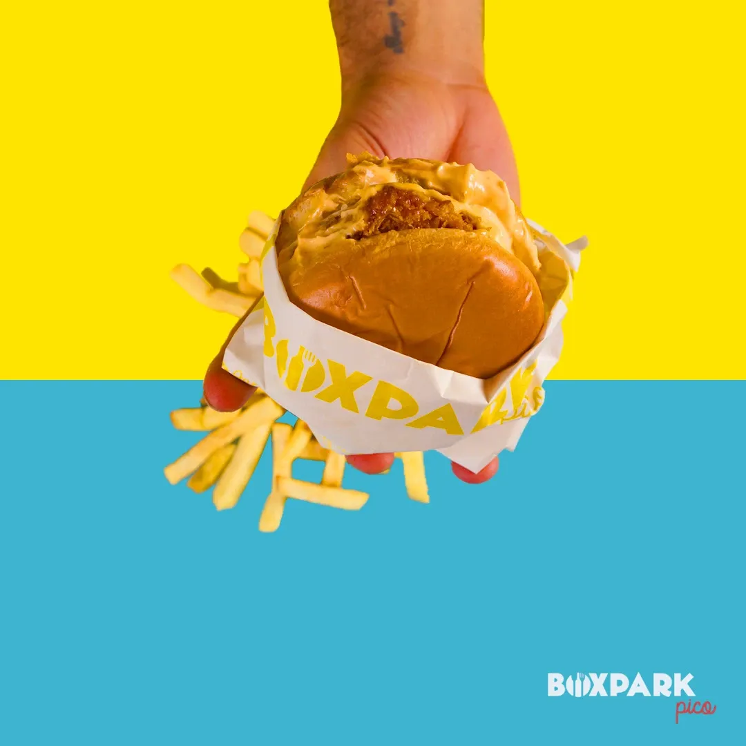 A hand holding a burger over a yellow and cyan field