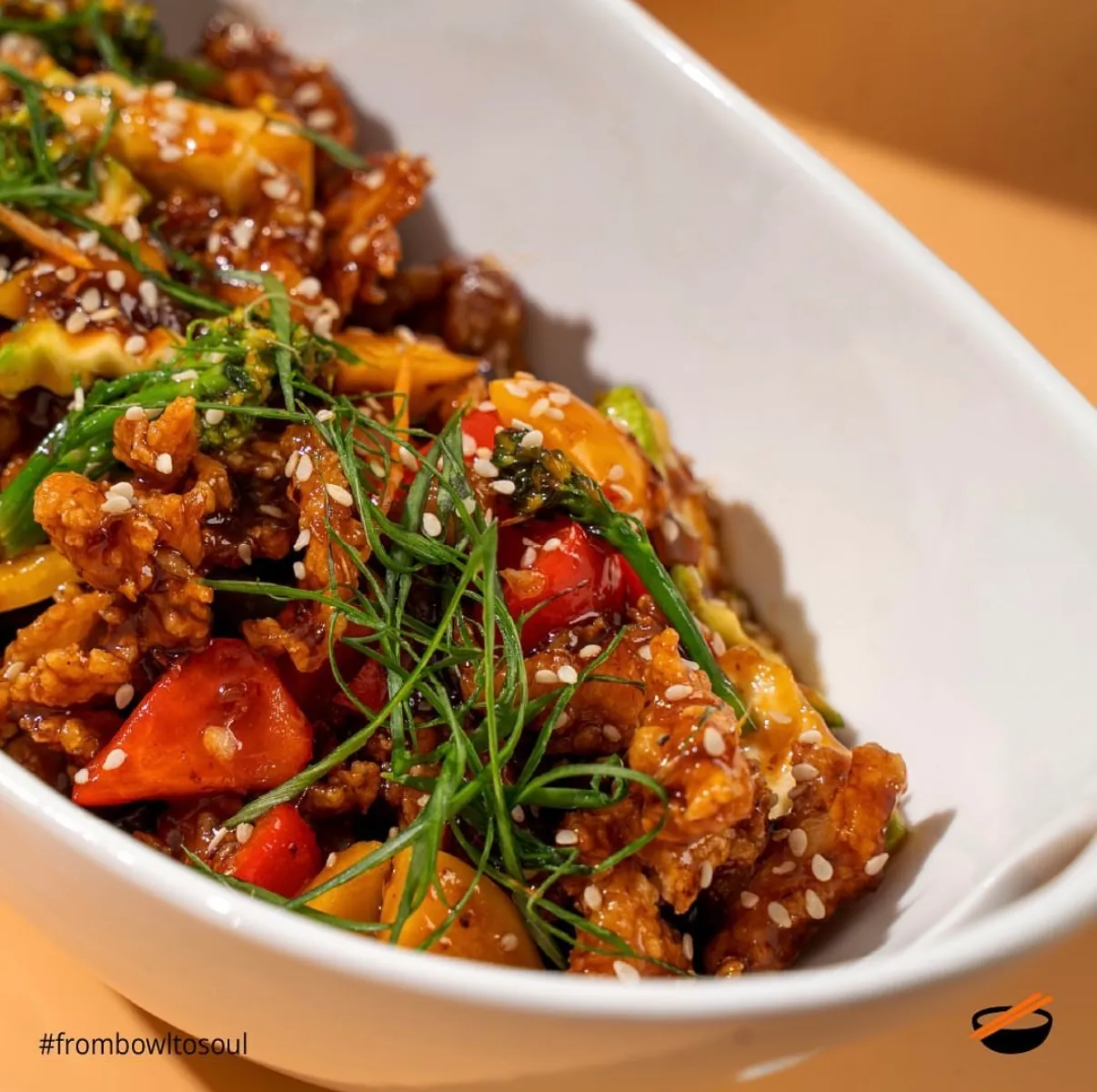 Close crop of chilli chicken with sesame and spring onion in a white bowl