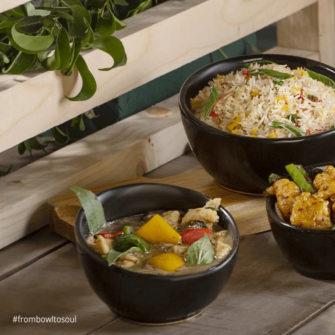 Dark bowls of rice, noodles and entrees arranged on a wooden table