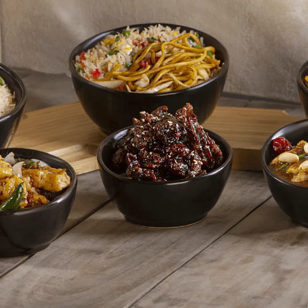 Bowls of chowmein, fried rice and chicken entrees on a wooden surface