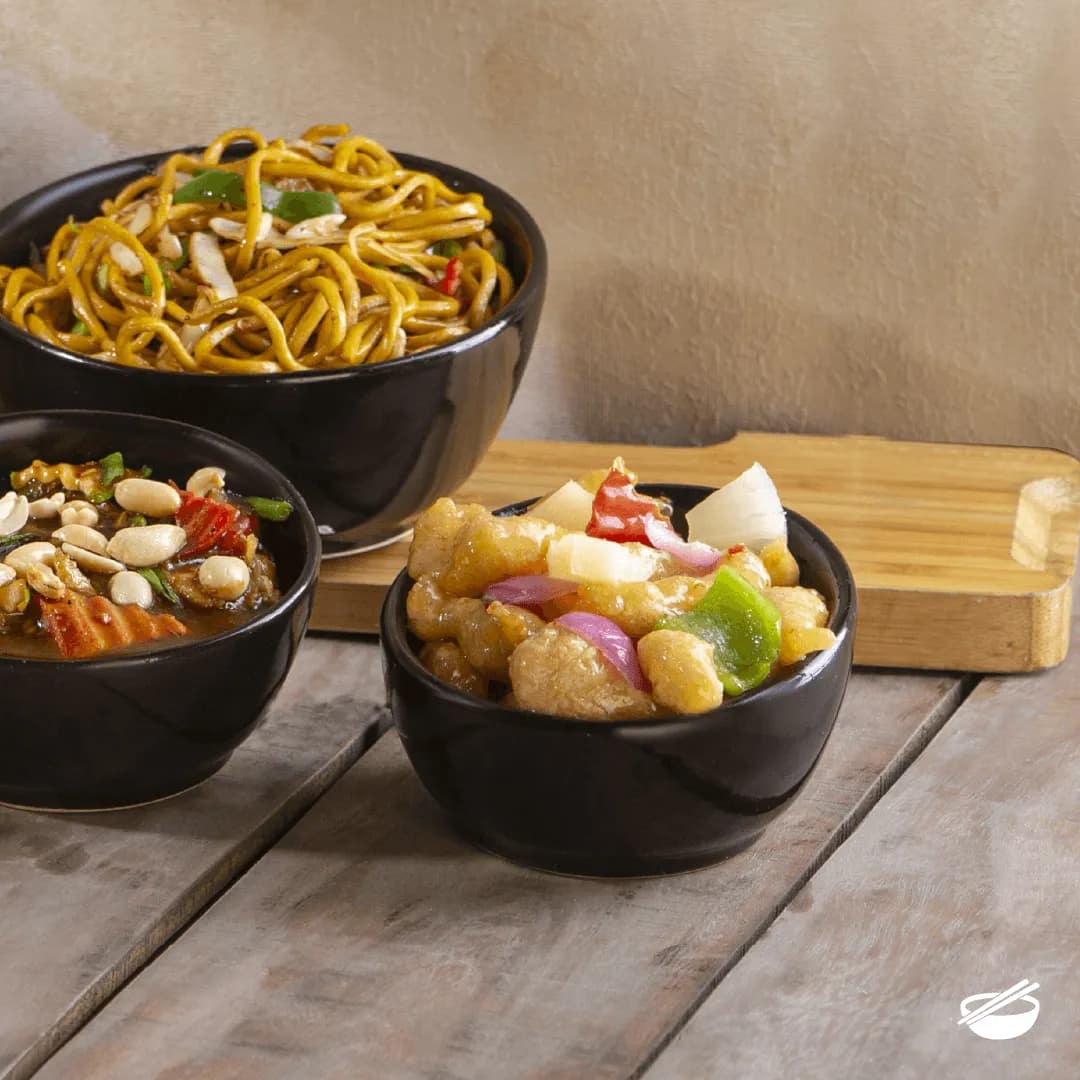 A spread of Chinese dishes in dark bowls on a wooden board