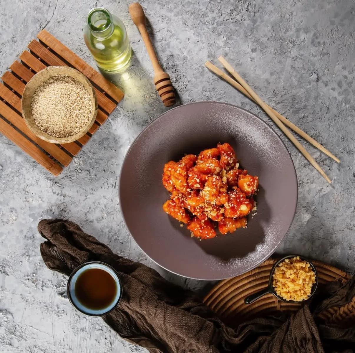 Overhead styled shot of a chicken dish with sesame, sauces and chopsticks