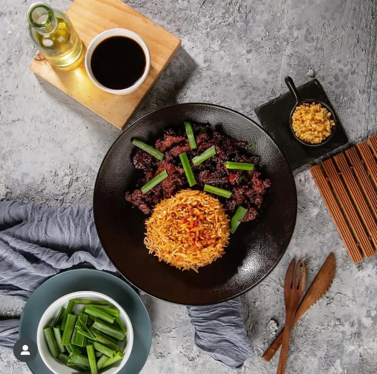 Beef and noodles plated dark, styled with spring onion and side dishes