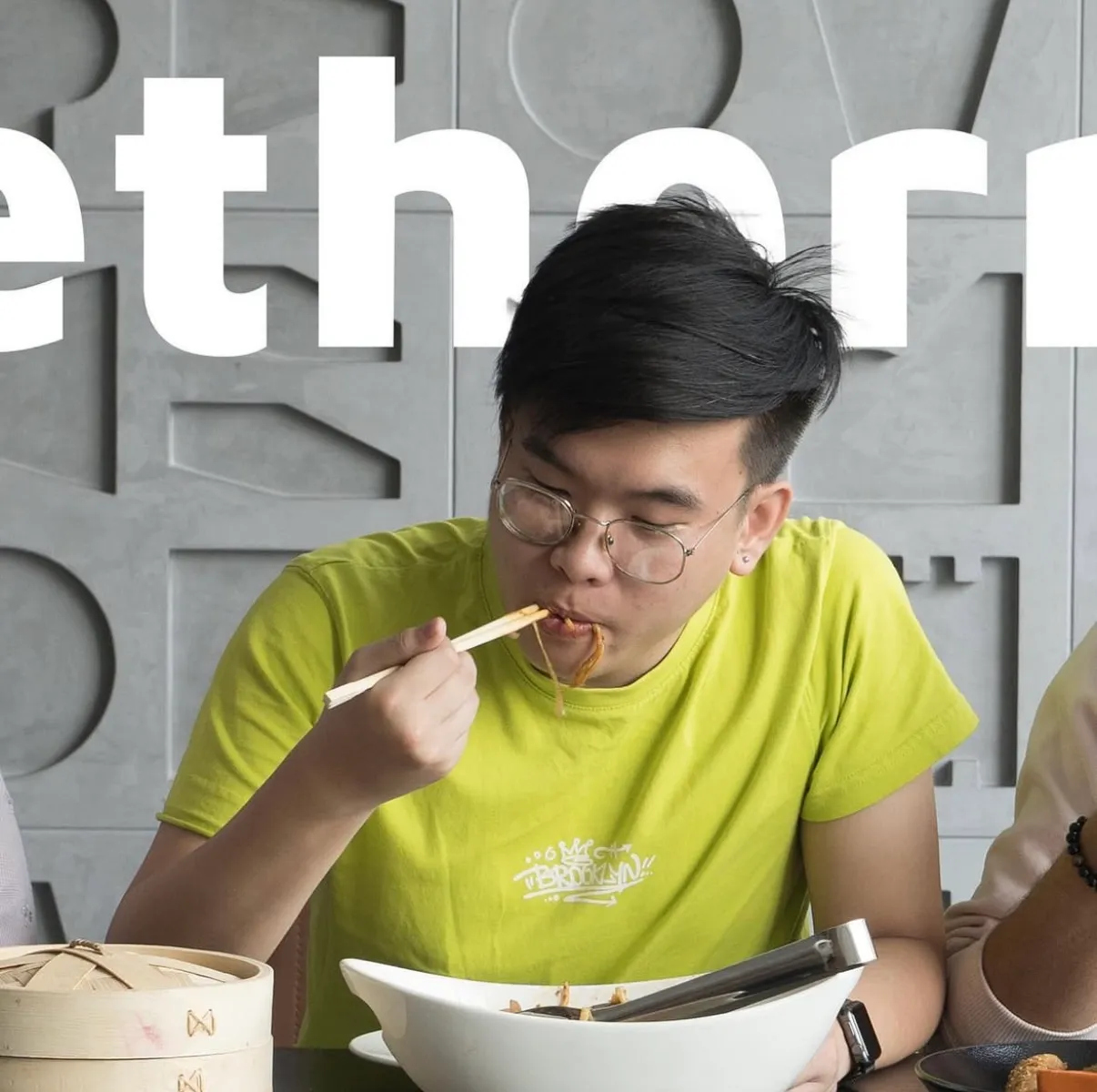 A man in a green shirt eating noodles with chopsticks, centre panel of the togetherness triptych